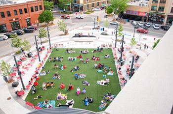A large group of people are sitting on a grassy area in the middle of a city square.